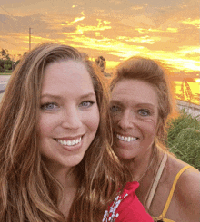 two women posing for a picture with the sun setting in the background