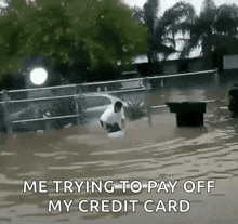 a man is standing in a flooded parking lot holding a bucket of water while trying to pay off his credit card .