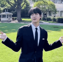 a young man in a suit and tie is standing in front of a white house with his arms outstretched .