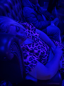 a woman wearing a leopard print shirt is sleeping on a couch