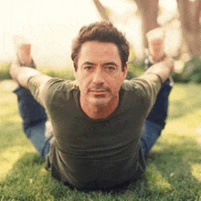 a man in a green shirt is doing a yoga pose on the grass .