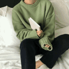 a person wearing a green sweater is sitting on a bed with a book