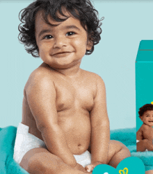 a baby in a diaper is sitting next to a box of pampers