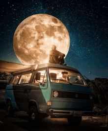 a man sitting on top of a van with a full moon behind him