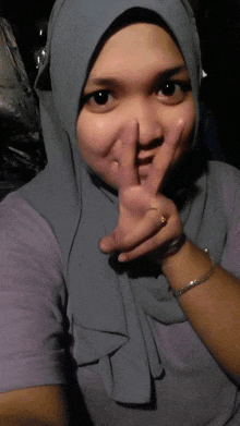 a woman wearing a hijab holds her finger to her nose