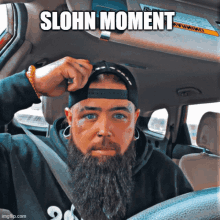 a man with a beard is sitting in a car with the caption " slohn moment " on the bottom