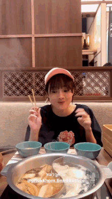 a girl is sitting at a table with bowls of food and chopsticks in front of a pot of food