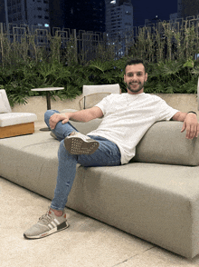 a man sitting on a couch wearing a white shirt and blue jeans