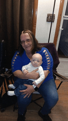 a woman in a blue shirt holds a baby in her arms