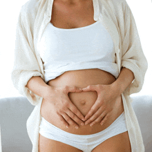 a pregnant woman making a heart with her hands on her belly