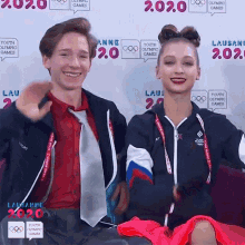 a man and a woman are posing for a photo in front of a wall that says youth olympic games