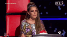 a woman in a sequined dress is sitting at a desk with a red button in front of her .