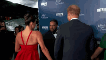 a man in a tuxedo stands next to a woman in a red dress in front of a wall that says intrepid