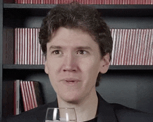 a man holds a glass in front of a bookshelf that has a book titled " a brief history of the world "