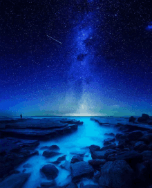 a person standing on a rocky beach under a starry sky