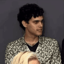 a man in a leopard print shirt is sitting next to a woman in a crowd .