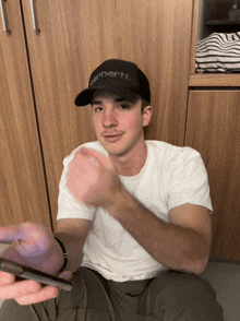 a man wearing a black carhartt hat holds a phone