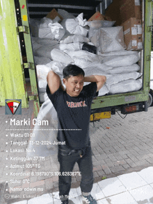 a man is carrying a heavy load in front of a truck that says marki cam on the back