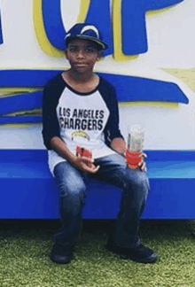 a boy wearing a los angeles chargers shirt is sitting on a blue bench