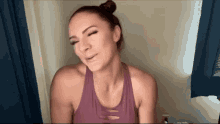 a woman in a purple tank top is making a funny face while standing in front of a window .