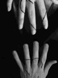 a black and white photo of a person holding another person 's hand with a string between them .