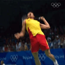 a man in a yellow shirt and red shorts is playing badminton in front of a sign that says beijing 2008