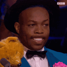 a man in a blue suit and bow tie is smiling and holding a stuffed animal with bbc written on the bottom