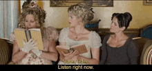 three women are sitting on a couch and one of them is reading a book and the other two are listening