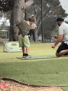 a man kneeling next to a young boy who is playing golf