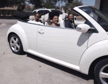 a woman and two children are in a white convertible car