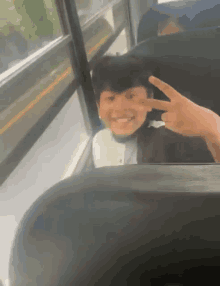 a young boy is sitting on a bus giving a peace sign