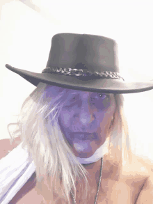 a woman wearing a cowboy hat and a white scarf has purple paint on her face