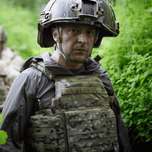 a man wearing a helmet and a bullet proof vest stands in the woods