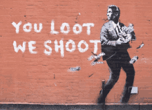 a brick wall with a painting of a man holding money and the words " you loot we shoot "