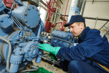 a man wearing blue overalls and green gloves is working on a machine