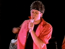 a man in a red shirt is singing into a microphone and dancing .