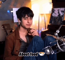 a young man is sitting in front of a microphone with his legs crossed and a bowl of food in front of him .