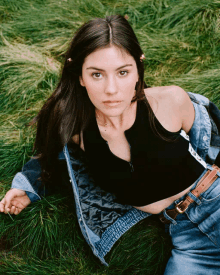 a woman wearing a black top and a denim jacket laying in the grass