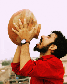 a man wearing a watch is drinking from a large clay pot