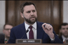 a man in a suit and tie speaking into a microphone with a name plate that says mr. vance on it