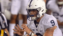 a football player wearing a white helmet and number 9 jersey is sitting on the field with his hands outstretched .