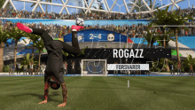 a soccer player is doing a handstand in front of a scoreboard that says rogazz