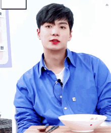 a young man in a blue shirt sits at a table with a bowl of food in front of him