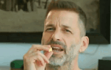 a man with a beard is eating a small piece of food with his mouth open .