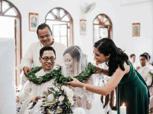 a woman in a green dress helps a bride and groom with their garland