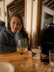 a woman sits at a table with two glasses of water and a glass of wine