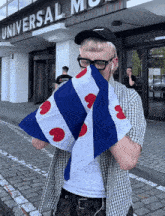 a man covering his face with a blue and white flag in front of a building that says universal music