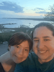 a woman and a child are posing for a picture in front of the ocean