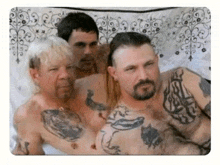 three shirtless men with tattoos on their chests pose for a picture