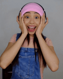 a woman wearing headphones and a pink headband holds her hands to her face